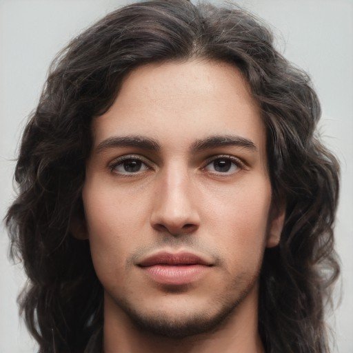 Man in his 20s with olive toned skin, long brown hair, and dark eyes